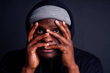 Endişeli genç Afrikalı Amerikalı mele gri şapkalı ve kapüşonlu siyah kapüşonlu tecavüzcünün saldırganından saklanıyor.