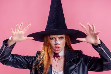 Büyük bir cadı şapkası ve siyah deri ceket giymiş kızıl saçlı kız. Stüdyo pembe arka planda burun ve boyun bandajı kırığı oluşturan ürkütücü kan.