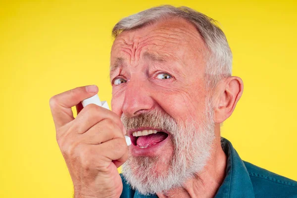 Hombre mayor usando un inhalador de asma en el estudio de fondo amarillo —  Fotos de Stock