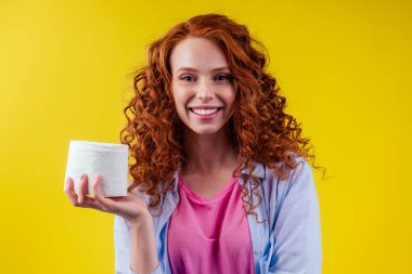 Kızıl saçlı, kıvırcık saçlı, kızıl saçlı, stüdyo sarı arka planında hijyen kağıdı olan bir kadın.