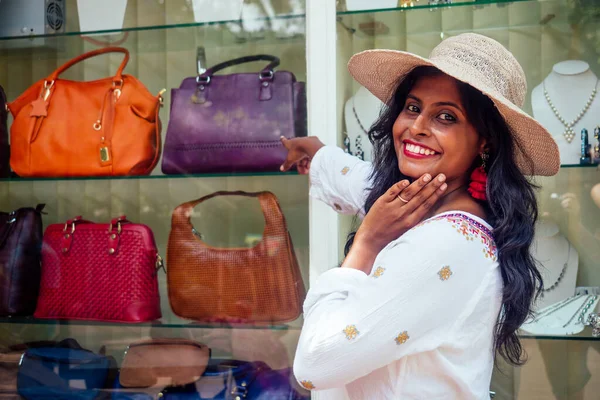 Glückliche indische Frau mit Strohhut und Stand in der Nähe der Vitrine mit Modetaschen in Indien Goa Markt — Stockfoto