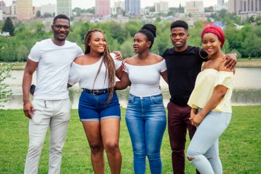 Beş gülümseyen Afro-Amerikalı kadın ve erkek göl kenarında bulutlu havada yürüyorlar, Rusya 'da değişim öğrencileri.