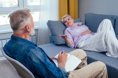 Güzel, kısa saçlı, goog görünümlü bir kadın kanepeye uzanmış, yaşlı bir sanatçı onun yanında oturuyor ve gündüz vakti oturma odasında büyük pencereli çizimler yapıyor.