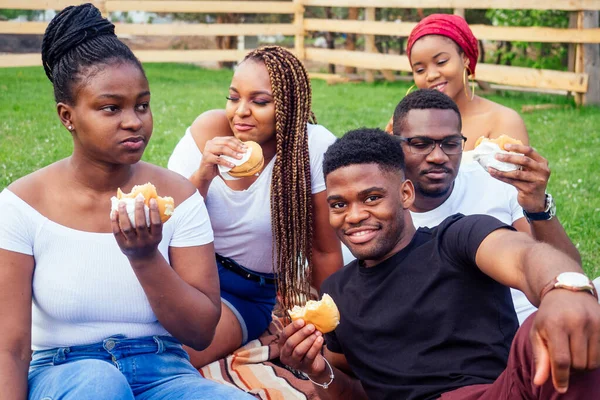 Happy casual america african people having fun and eating burger outdoors lifestyle,students for a break summer evening cloudy weather in park — Stock Photo, Image