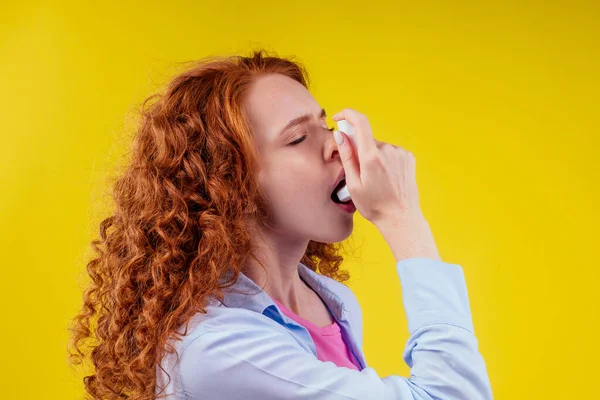 Upsad pelirroja rizado jengibre turista estudiante en una camisa azul que tiene asma usando el inhalador de asma por ser saludable amarillo fondo estudio — Foto de Stock