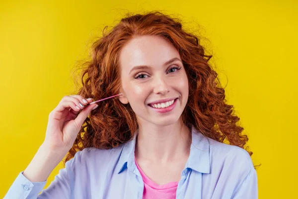 Lockigt rödhårig kaukasisk kvinna använder öron pinnar i studio gul bakgrund — Stockfoto