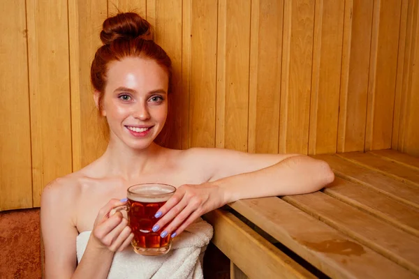 Pelirroja pelirroja mujer humeante en la casa de baños con escoba grupo ruso bebiendo beers.she disfrutar de la sauna finlandés spa — Foto de Stock