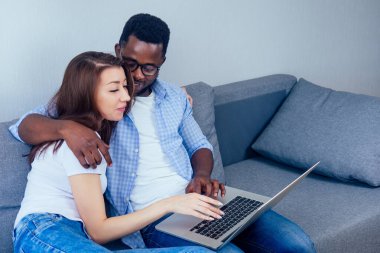 Uluslararası çift evde dinlenirken dizüstü bilgisayara bakıp gülümsüyor