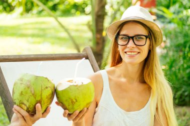 Genç çift güverte sandalyesinin altında otururken hindistan cevizi içer.