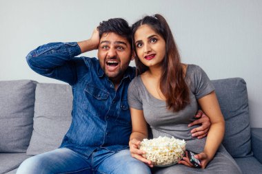 Genç Hintli çift ellerinde patlamış mısırla uzaktan kumandayla gerilim filmi izliyor.