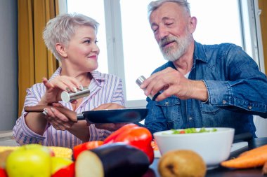 Kıdemli çift organik meyve ve sebzelerle vejetaryen yemeği hazırlıyor, tavaya tuz koyuyorlar.