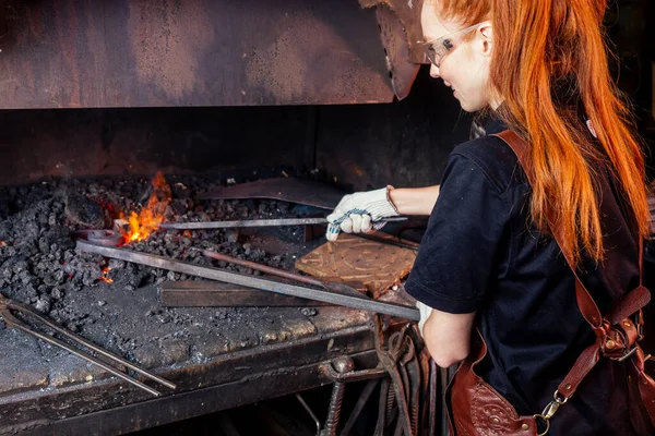 Vörös hajú gyömbér fiatal európai feminista nő visel bőr kötény dolgozó kovács műhely.kisvállalkozás erős és független koncepció — Stock Fotó