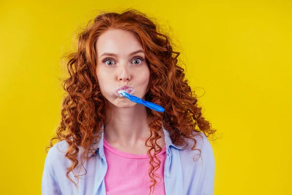 Somnoliento pelirroja mujer cepillarse los dientes con pasta de dientes eco pasta en amarillo estudio fondo — Foto de Stock