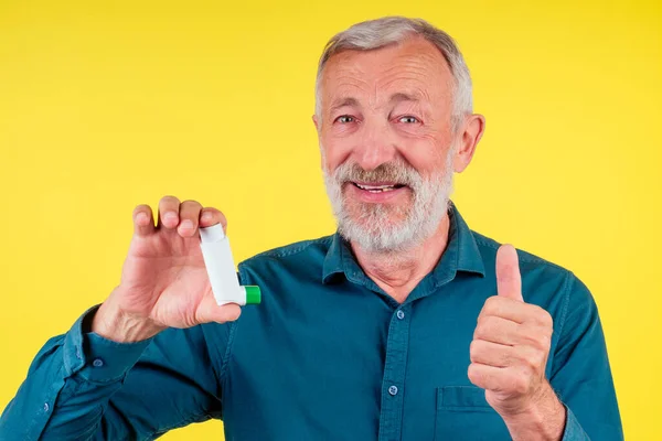 Hombre mayor usando un inhalador de asma en el estudio de fondo amarillo —  Fotos de Stock