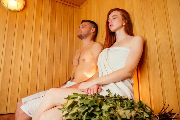 Pelirroja pelirroja mujer y su novio humeante en la casa de baños con el grupo ruso broom.couple en el amor disfrutando de la sauna juntos en el spa — Foto de Stock