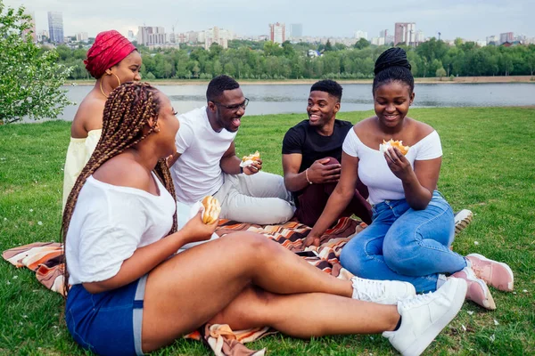 Happy casual america african people having fun and eating burger outdoors lifestyle,students for a break summer evening cloudy weather in park — Stock Photo, Image