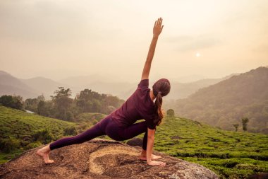 Menekşe kumaşlı kadın Munnar Hill Kerala Hindistan 'daki çay tarlalarında yoga yapıyor.