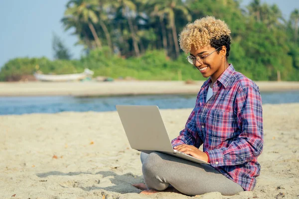 Glad latinska frilansande kvinna med blonda afro lockar sitter på tom strand med laptop palmer bakgrund. fjärrdröm bästa arbetskoncept — Stockfoto