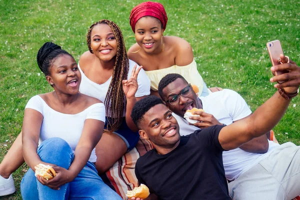 Grupo de cinco amigos do sexo feminino e masculino tomando selfie no smartphone câmera e se divertindo ao ar livre estilo de vida perto do lago, comer piquenique hambúrguer no parque — Fotografia de Stock