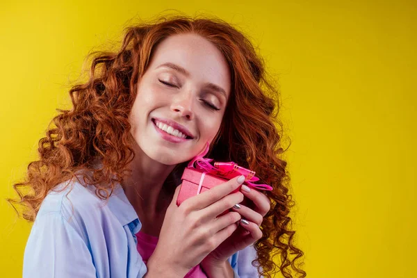 Rothaarige lockige Ingwerfrau hält Geschenkbox im Studio gelben Background.Mother Day und achten von Marchor St. Valentinstag Konzept — Stockfoto