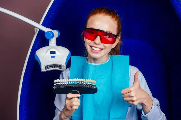 Dentist works on tooth crown in dental laboratory ultraviolet painting teeth with mineral and calcium cream to young red-haired ginger woman — Stock Photo, Image