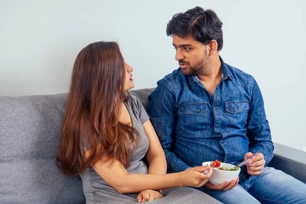 Young indian couple sitting in they living room and eating vegetable salad