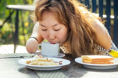 Güzel Asyalı kadın tropikal tatil köyünde kahvaltı yapıyor. Bir fincan çay ya da kahve içiyor.