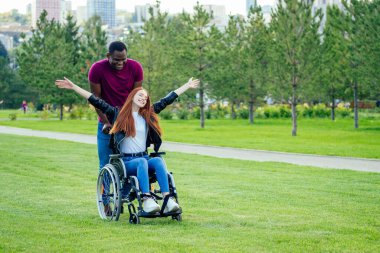 Afro-Amerikan erkek evlilik teklifi kızıl saçlı kız arkadaşına yüzük veriyor. Tekerlekli sandalyede oturuyor ve şaşırmış ve şaşırmış.