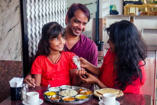 Father ,mother and little girl using wash hand sanitizer gel before eating in india cafe