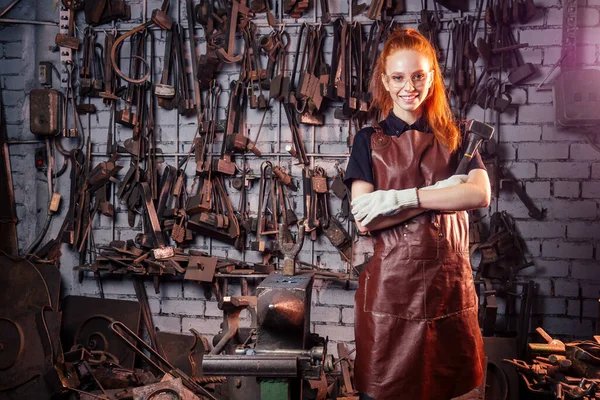 Redhaired gengibre jovem mulher feminista europeia vestindo avental de couro trabalhando blacksmith workshop.small empresa conceito forte e independente — Fotografia de Stock