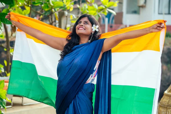 Hermosa mujer sosteniendo bandera india tricolor, usando sari tradición azul en la playa del mar en Goa —  Fotos de Stock