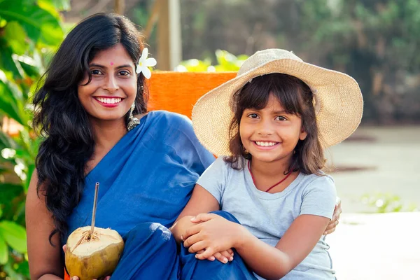 Счастливая дочь в соломенной шляпе со своей прекрасной матерью в голубом сари, пьющей свежую кокосовую воду на тропическом райском пляже Гоа. использование экологически чистых труб для переработки металла — стоковое фото