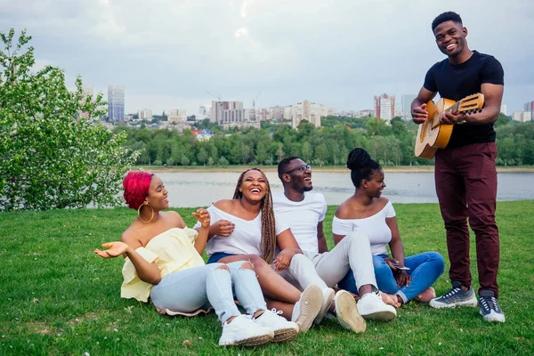 Group of smiling happy afro-american friends friends playing guitar outdoors picnic in the campaign — Stock Photo, Image