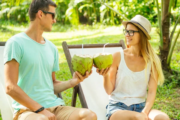 Jovem casal amoroso beber coco enquanto sentado sob palmas na espreguiçadeira lounge resort — Fotografia de Stock