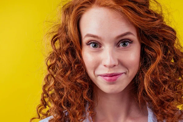 Счастливая беззаботная молодая рыжая женщина с рыжими кудрями хитрым взглядом на студийном жёлтом фоне — стоковое фото