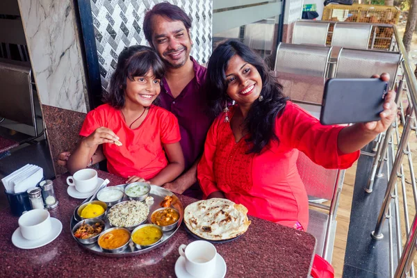 Красивая мать и счастливый отец есть тали с дочерью в кафе и пить чай Масала и делать селфи фото на смартфоне камеры — стоковое фото