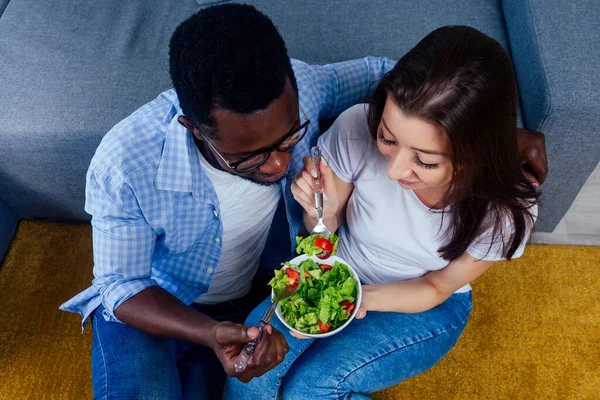Hombre afroamericano comiendo ensalada con mujer en sala de estar — Foto de Stock