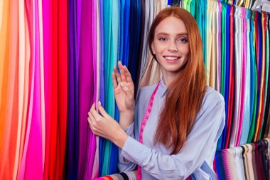 redhair ginger woman choosing color textile in tailor shop for new cloth sewing.she determines the colors that best suit an individual based capsule wardrobe clipart