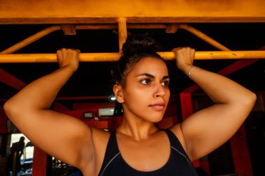 Latin Amerikalı, kaslı, iri omuzlu kız spor salonunda barfiks çekiyor.