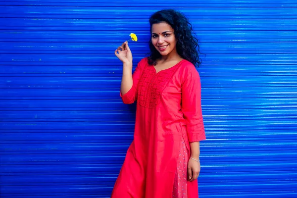 Atractiva hermosa feliz joven latina hispana con bindi de teca en la frente sonriendo en fondo azul de la calle de la pared sosteniendo flover fresco —  Fotos de Stock