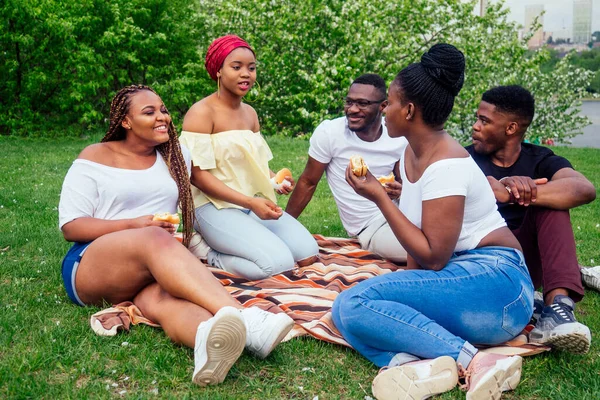 Feliz casual america Africano pessoas se divertindo e comer hambúrguer ao ar livre estilo de vida, estudantes para uma pausa verão noite nublado tempo no parque — Fotografia de Stock