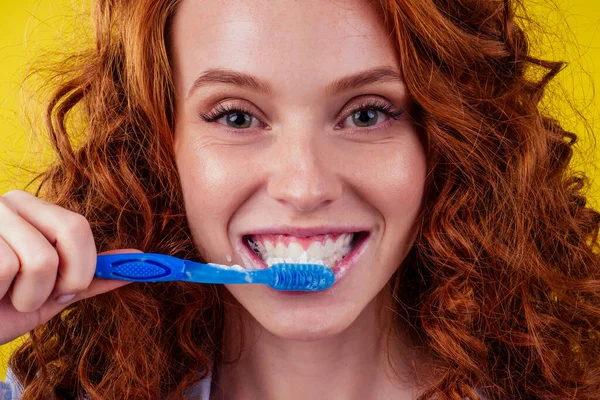 Redhaired ginger woman brushing teeth with toothpaste eco paste on yellow studio background — Stock Photo, Image