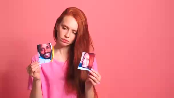 Pelirroja pelirroja mujer en rosa estudio de fondo rasgando tarjeta de fotos de sonriente pareja internacional — Vídeos de Stock