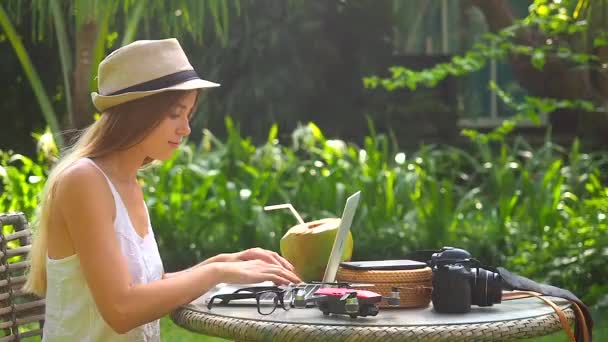 ブロンドの女性は麦藁帽子をかぶって熱帯の場所で働いてココナッツを飲む — ストック動画