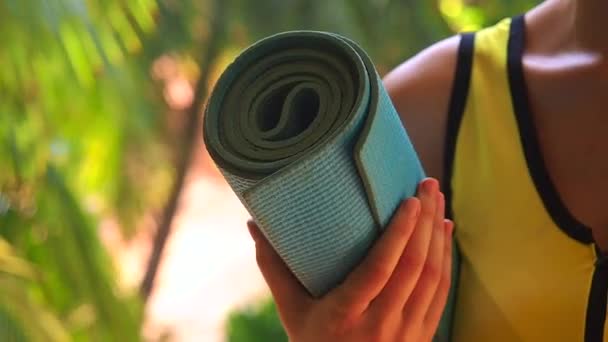 Mujer joven sosteniendo rollo yoga mat afuera en entorno natural — Vídeos de Stock