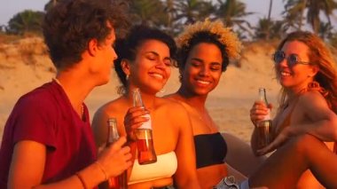 Afro-Amerikan, Hint ve Kafkas grubu gün batımında sahilde limonata içiyor.