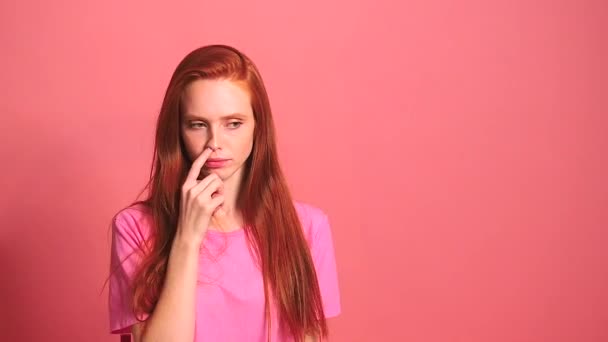Rödhårig ingefära kvinna i rosa studio bakgrund plockar hans näsa finger — Stockvideo