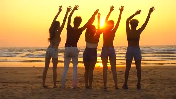 Gruppe glücklicher Menschen sitzt am leeren Strand bei Sonnenuntergang und winkt der Sonne zu — Stockvideo