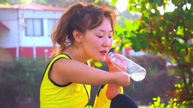 Mutlu Asyalı kolsuz kadın tropik sahilde yüzmeden önce ısınıyor. Bustadan su içiyor.