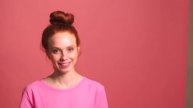 Pembe stüdyo arka planında kızıl saçlı kadın, kafası sallanırken topuzu parçalandı.